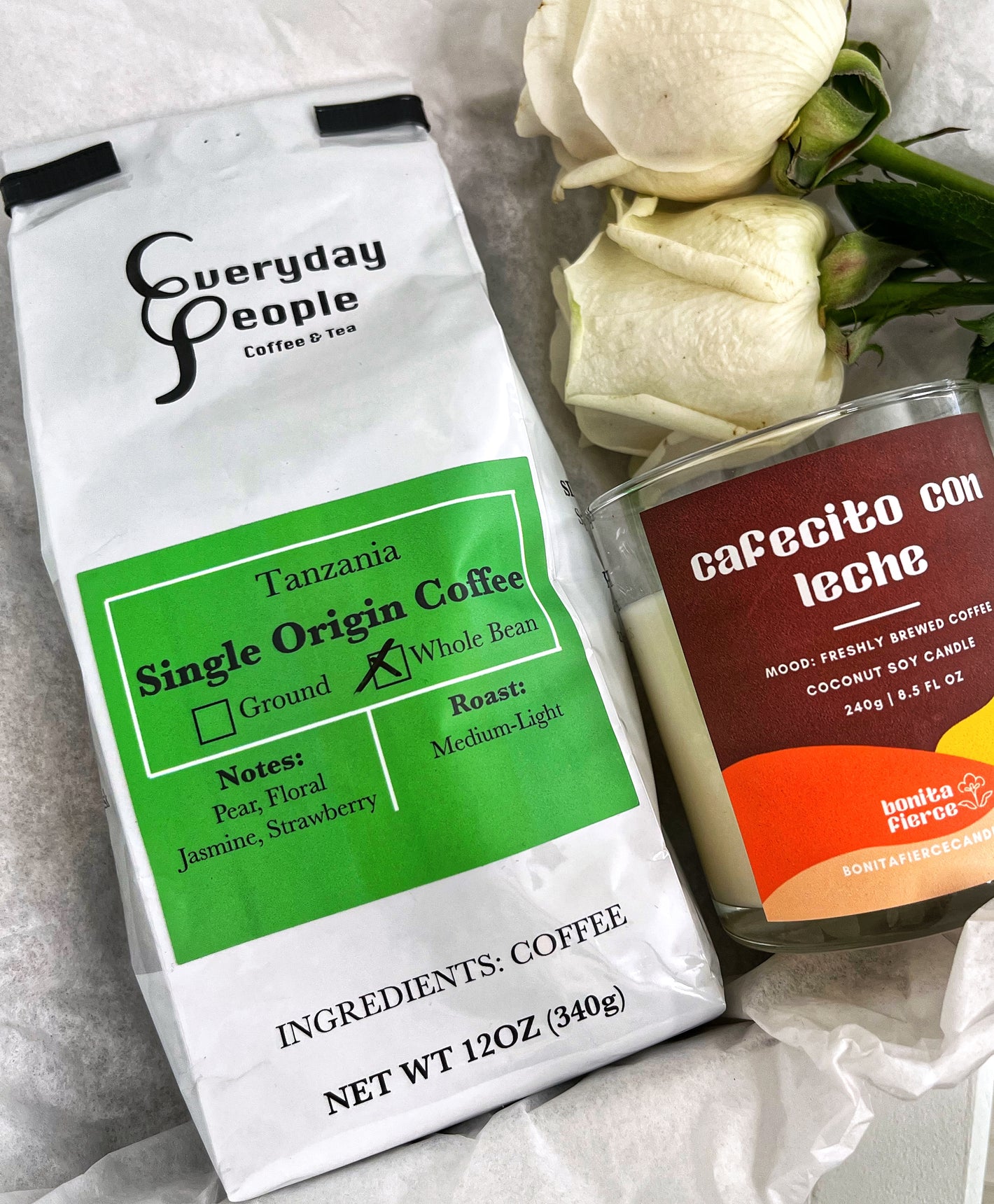 Products within Sueños Coffee Co's morning cafecito box. Pictured is a bag of specialty coffee from Everyday People Coffee & Tea, a Cafecito con Leche candle from Bonita Fierce and two white roses. 